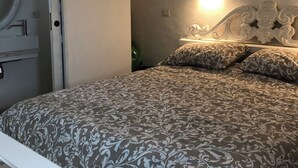 Une chambre à coucher avec un lit, une table de chevet, une lampe fixée au mur et une porte.