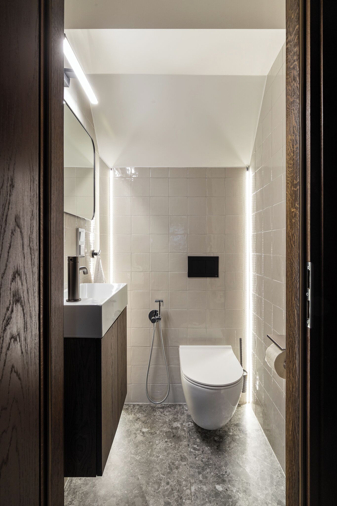 A modern bathroom with a marble floor, a white toilet, a sink with a mirror, and a shower.