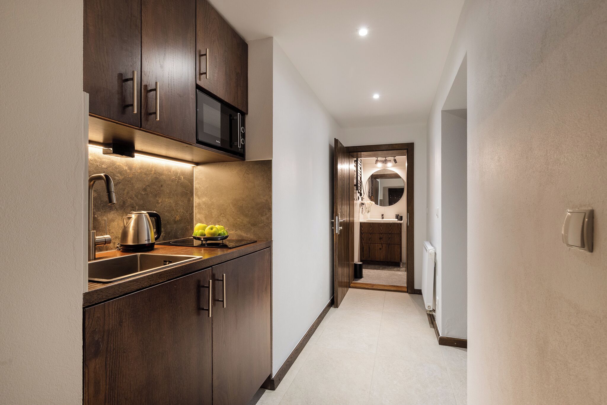 A modern kitchen with dark wood cabinets, a stainless steel kettle, and a microwave.