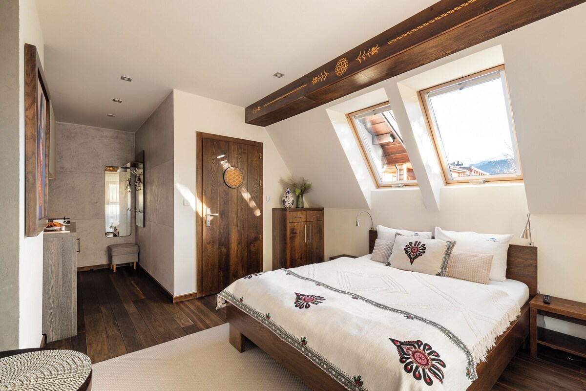 Un dormitorio con una cama grande, vigas de madera, un tragaluz y vistas al exterior.