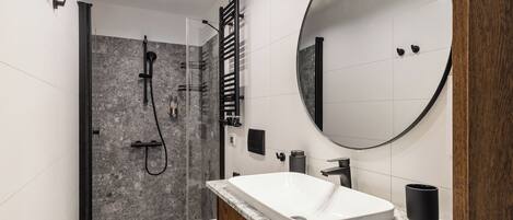 Un baño moderno con ducha, inodoro y tocador con un espejo grande.