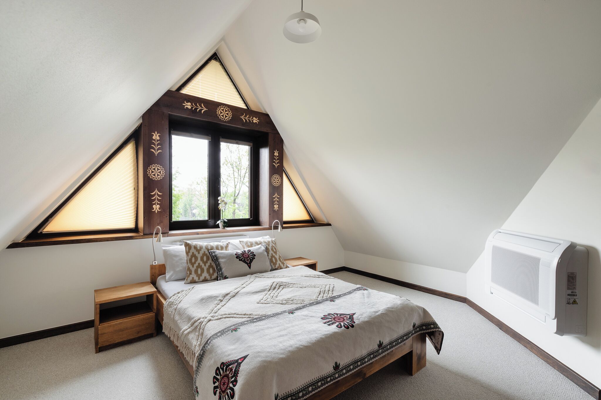 A bedroom with a sloped ceiling, a bed with patterned bedding, a bedside table, and a window with blinds.