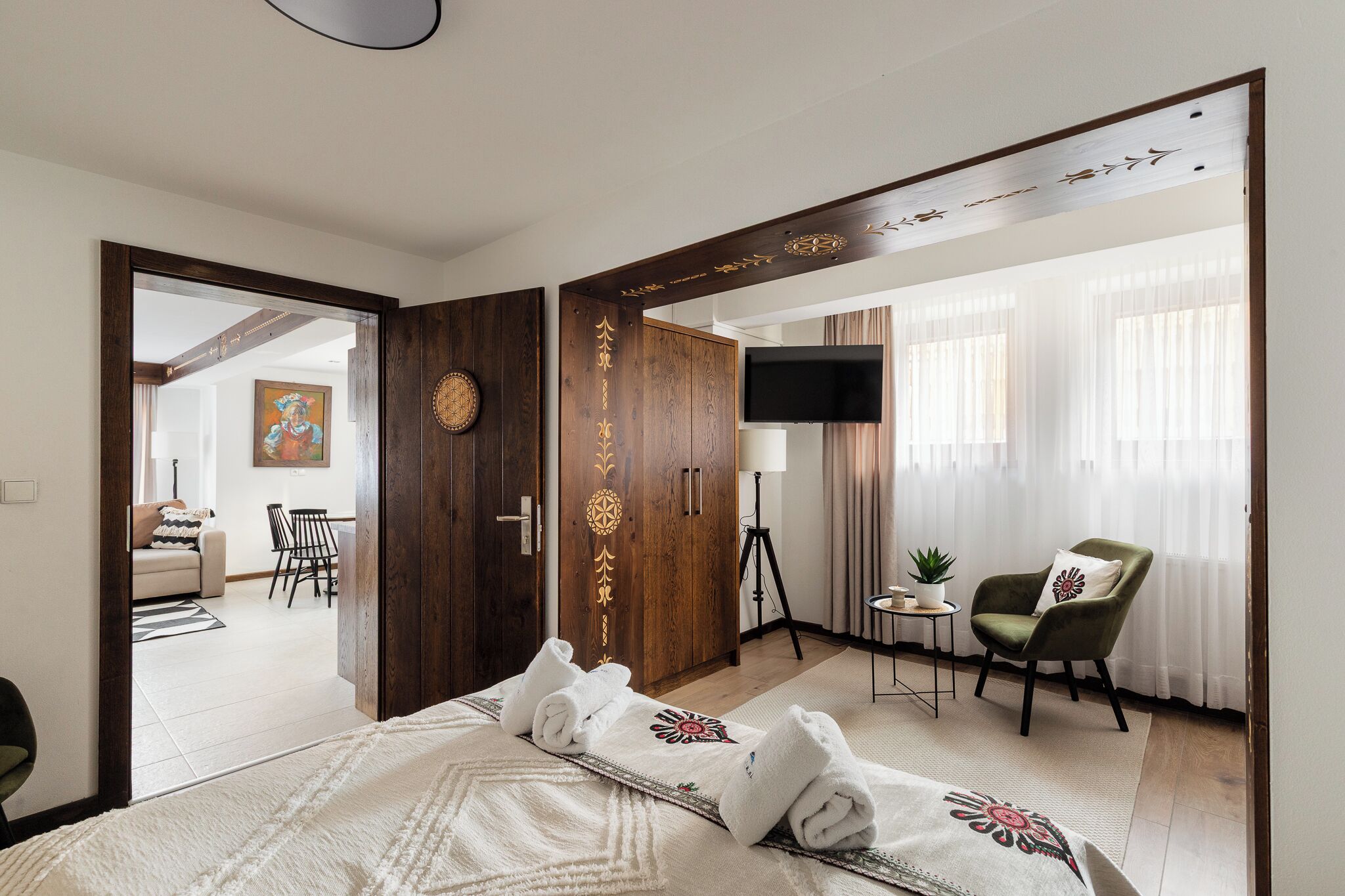 Quarto de hotel com cama, televisão, cadeira e secretária com candeeiro.