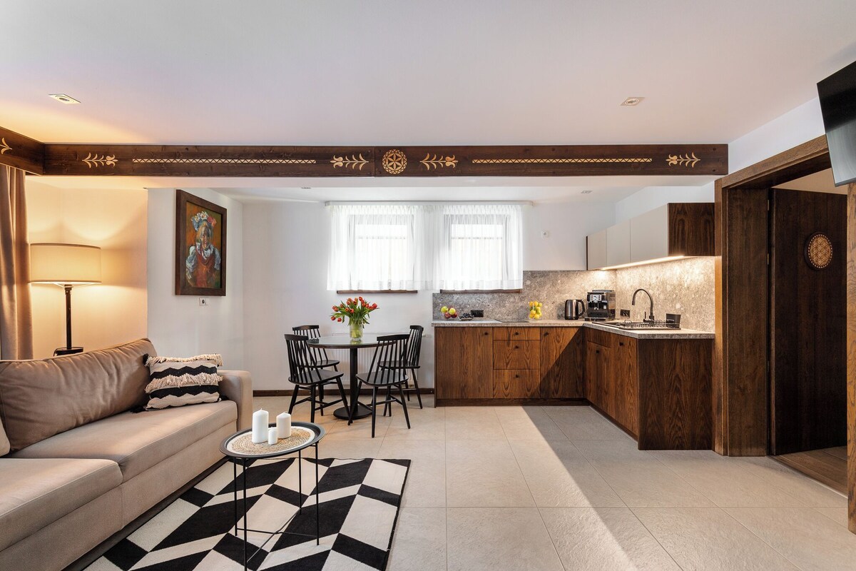 Una sala de estar moderna con un sofá, una mesa de comedor con sillas, una cocina con armarios de madera y un televisor montado en la pared.