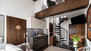 Un interior modern amb un sofà, una taula de dinar amb cadires, una zona de cuina i una escala.