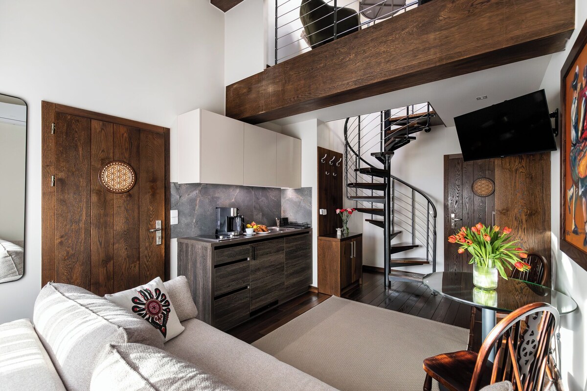 Un interior moderno con sofá, una mesa de comedor con sillas, una zona de cocina y una escalera.