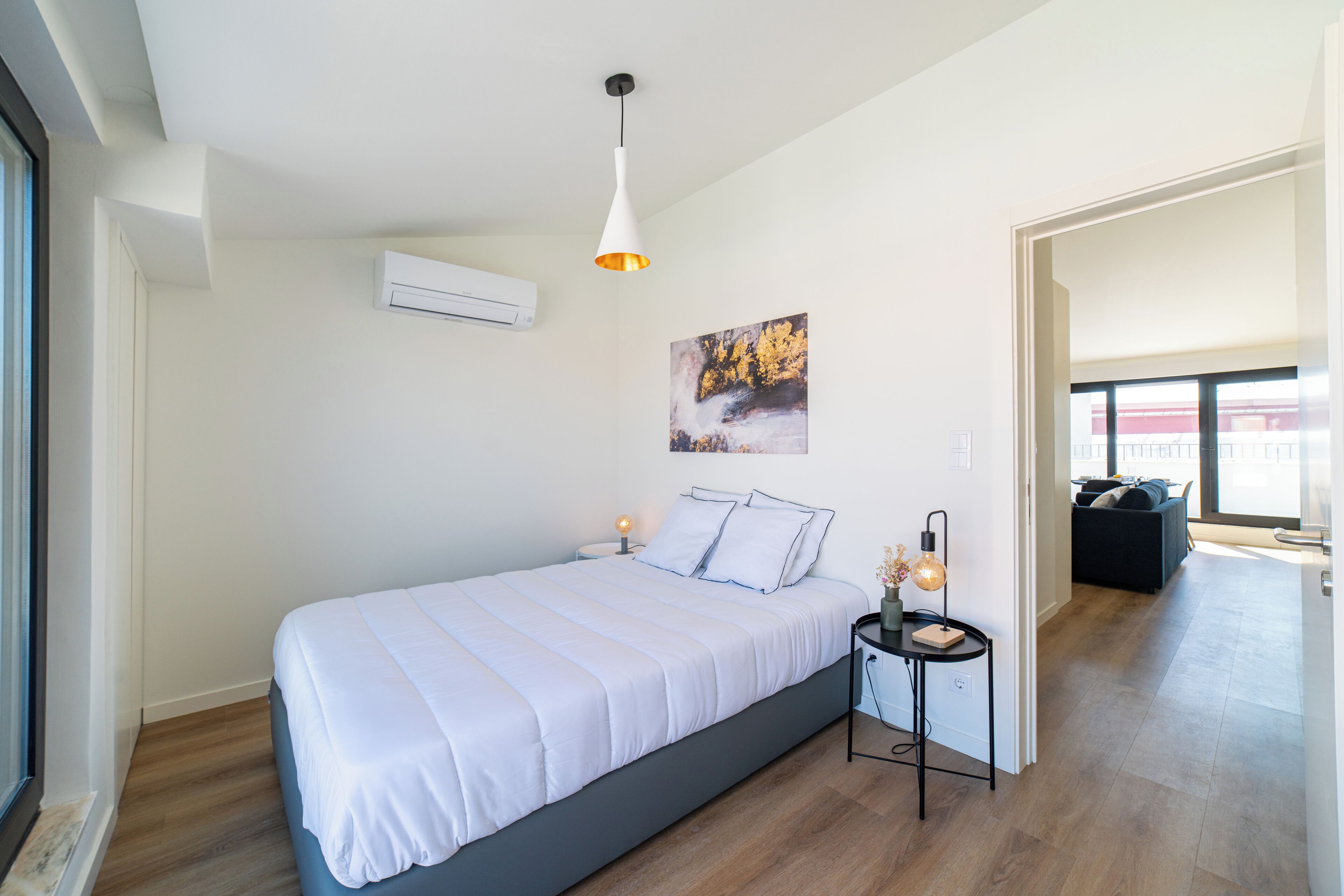 Quarto moderno com cama grande, mesa de cabeceira com abajur e pintura na parede.