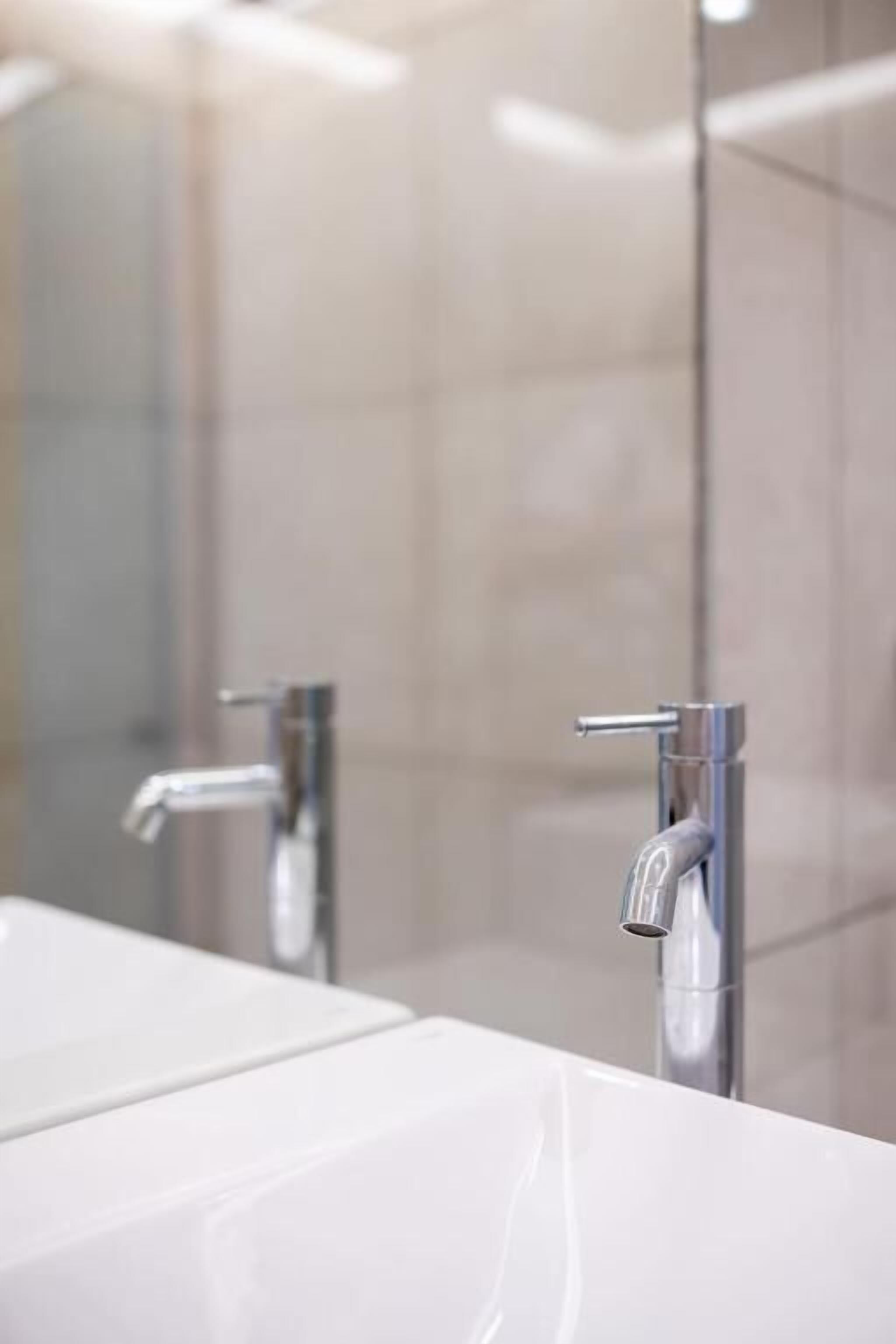Ein Badezimmer mit einem weißen Waschbecken, einem Spiegel und einem Chrom-Wasserhahn.