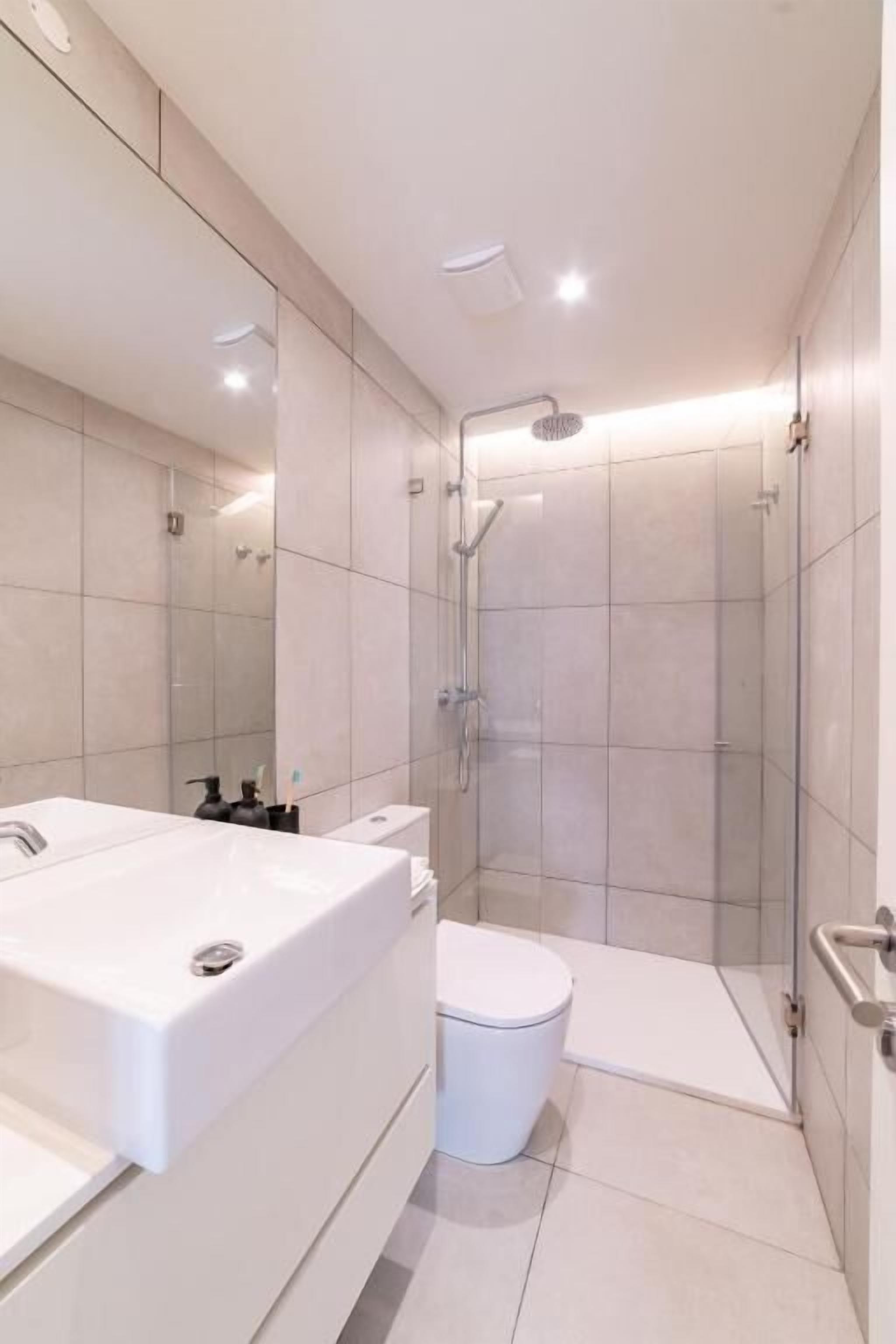 Un bagno moderno con un ampio lavandino bianco, un water e uno spazio doccia vetrato.