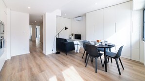 A modern kitchen with white cabinets, a dining area with a round table and chairs, and a black floor lamp. - Alcântara 2 (Lisbon)