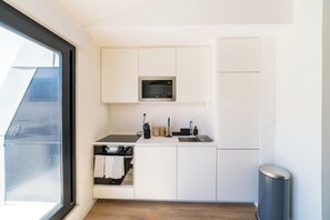 A compact kitchen with white cabinets, a built-in microwave, a sink, and a trash can. - Alcântara 2 (Lisbon)