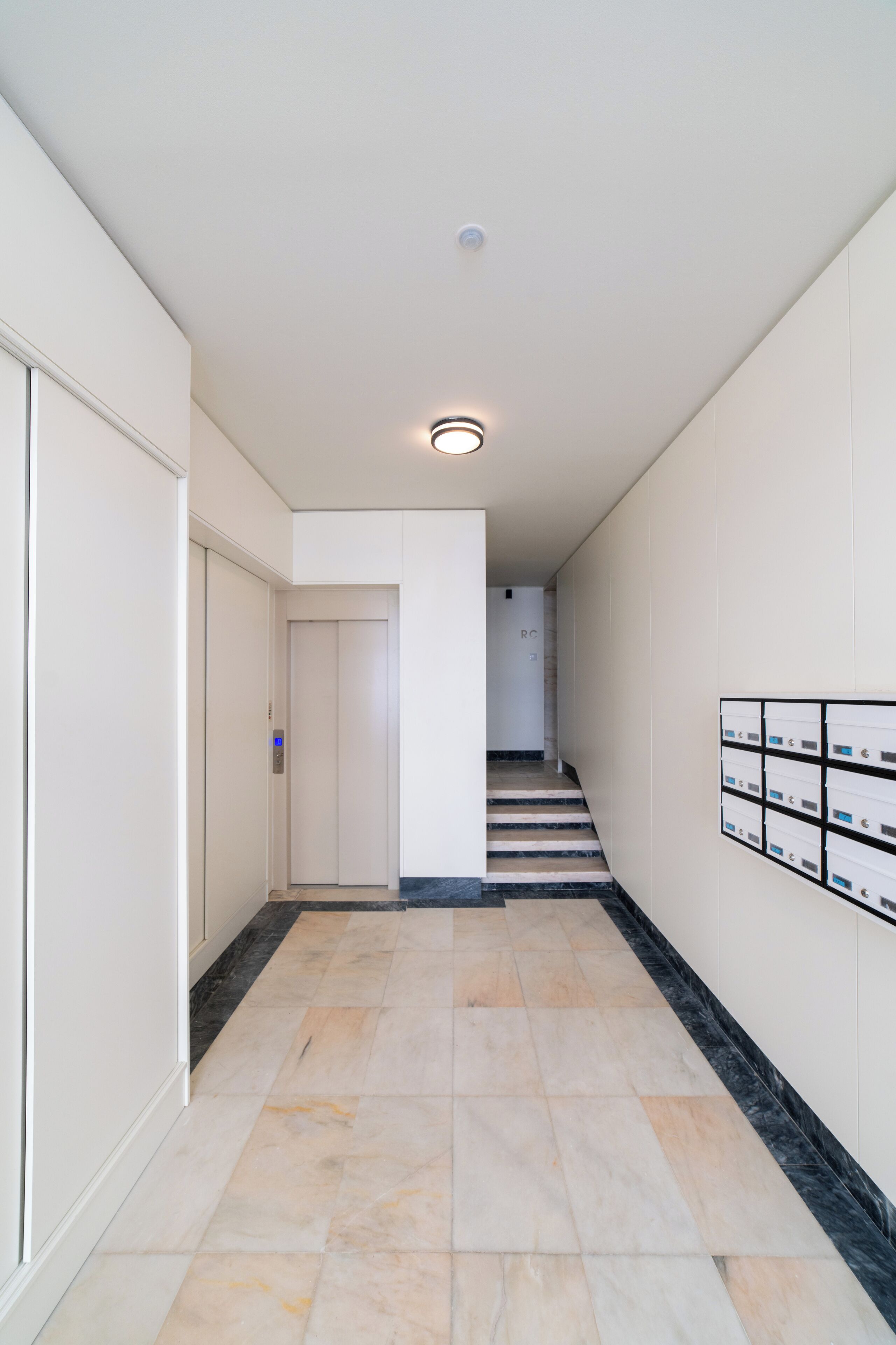 A hallway with a tiled floor, a staircase, and a wall-mounted mailbox.