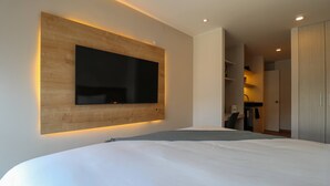 Une chambre à coucher moderne avec un grand lit, un téléviseur fixé au mur et un mur d’accent en bois.