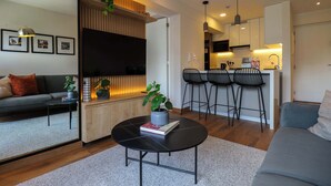 Un salon moderne avec un canapé, une table basse et un téléviseur. Il y a également un coin cuisine avec une table à manger et des tabourets de bar.
