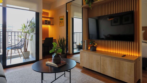 Un salon moderne avec une grande télévision, un canapé, une table basse et un balcon agrémenté de plantes.