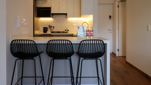 Une cuisine moderne avec des meubles blancs, un îlot central doté de tabourets et une machine à café.