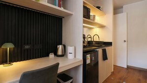 Une cuisine compacte équipée d’un four à micro-ondes, d’une bouilloire et d’un évier, ainsi que d’une petite poubelle et d’un bureau avec une lampe.