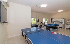 Une pièce équipée d’une table de ping-pong, d’une table de billard et d’un téléviseur fixé au mur.