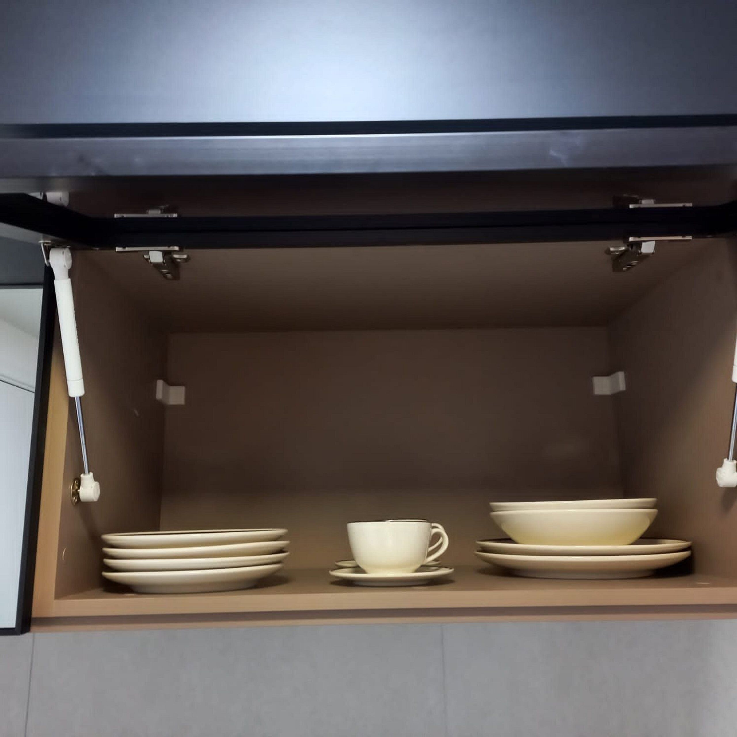 A kitchen cabinet with a built-in shelf containing stacked plates, a cup, and a bowl.