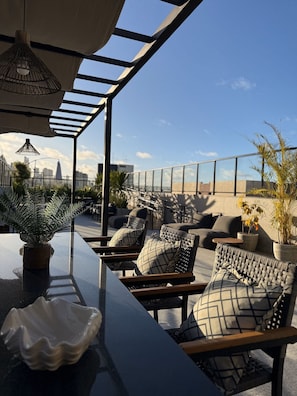 A rooftop terrace with outdoor seating, a bar area, and potted plants. - Flat Cabo Branco Aurea 50m do mar 602 (João Pessoa)