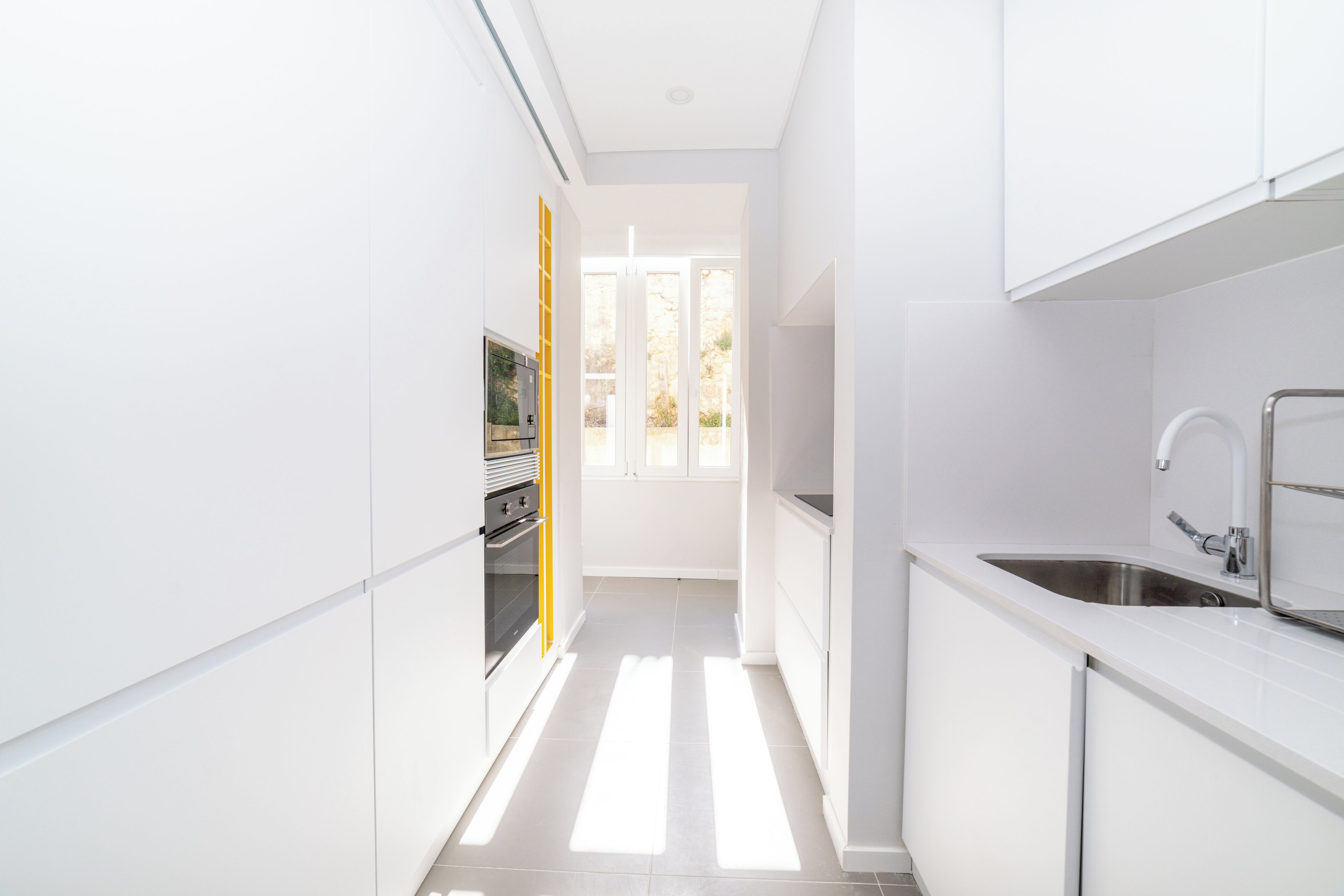 A modern kitchen with white cabinetry, a stainless steel sink, and a built-in oven.