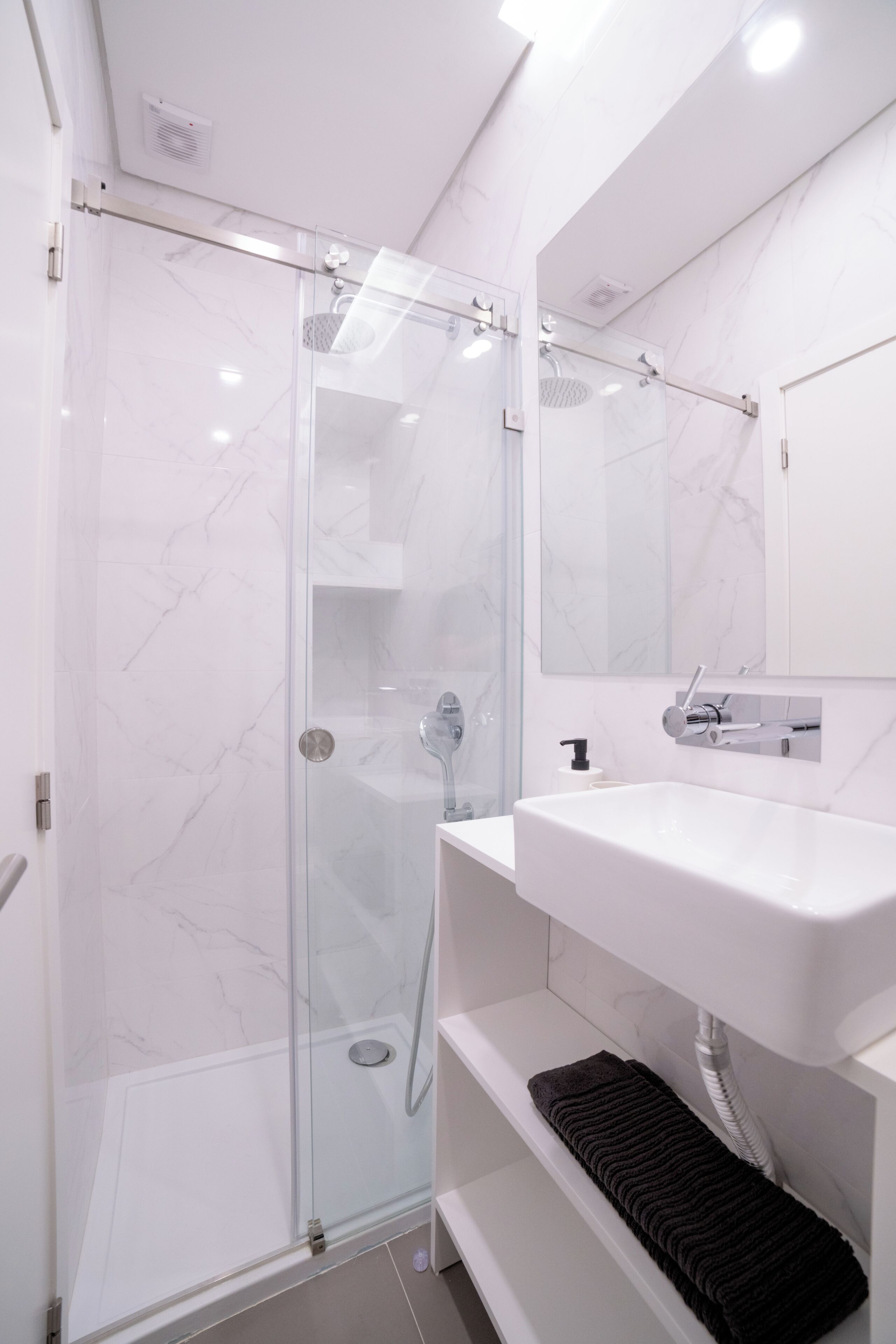 A modern bathroom with a glass-enclosed shower, a white sink, and a mirror above it.