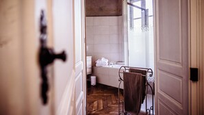Une salle de bain avec un plancher en bois disposé en motif de chevron, une baignoire blanche et un porte-serviettes avec une serviette marron.