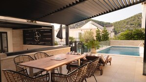 An outdoor patio with a wooden table and chairs, a pool, and a view of houses and hills in the background. - royale 3 with shared pool Hvar (Hvar)