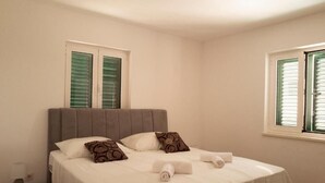 A neatly made bed with white linens and two pillows, a bedside table with a lamp, and a window with green shutters. - royale 3 with shared pool Hvar (Hvar)