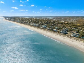 Een vogelvluchtperspectief van een kustgebied met woningen aan het strand, een heldere lucht en een rustige zee.