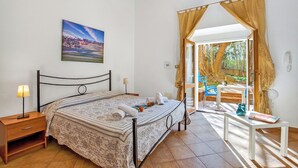 A bedroom with a bed, bedside table, lamp, and a painting on the wall. - Residence Argentiera Apartments (Sassari)