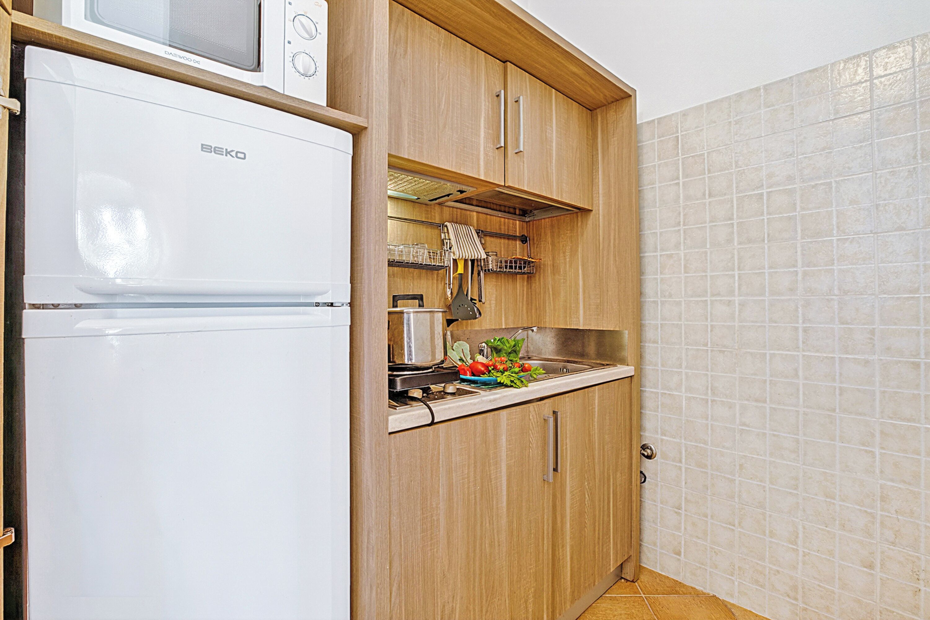 A compact kitchen with a white refrigerator, wooden cabinets, a microwave, and a sink.