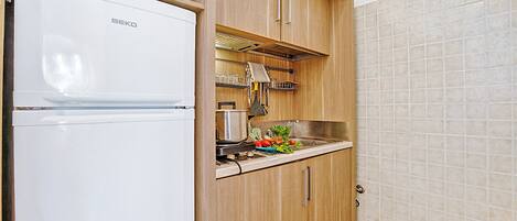 A compact kitchen with a white refrigerator, wooden cabinets, a microwave, and a sink.