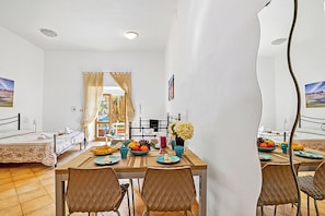 Una habitación con una cama, una mesa de comedor con sillas, un frutero y un jarrón con flores.