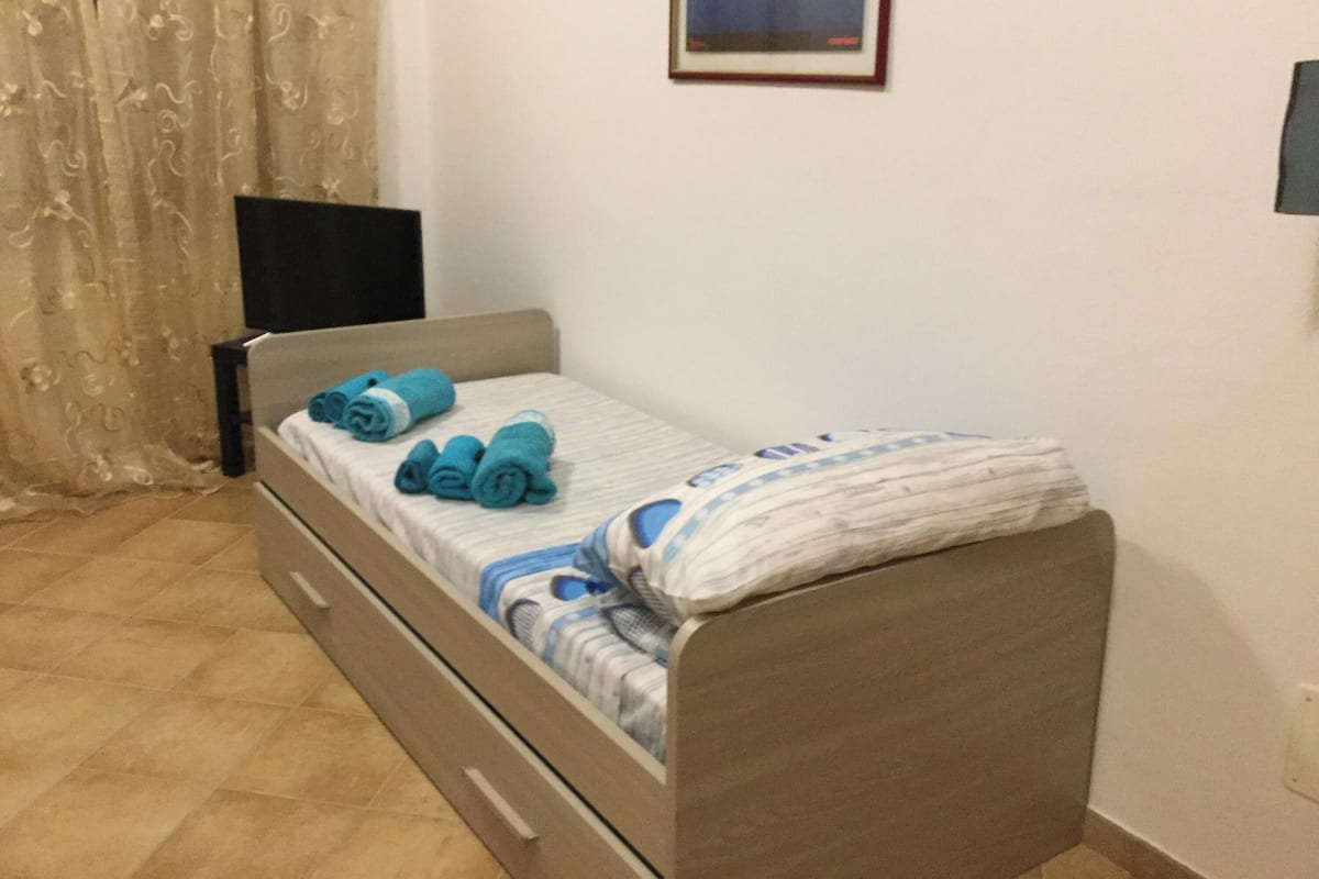 A single bed with a headboard, a bedside table, a drawer, and a wall-mounted TV.
