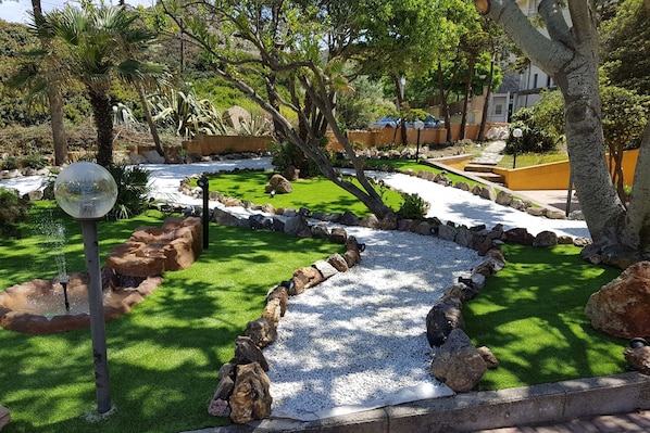 Un jardín ajardinado con fuente, rocas y un sendero.