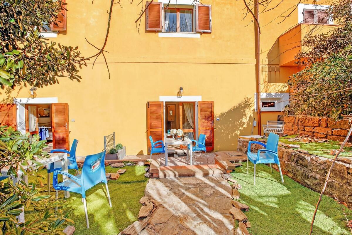 A yellow building with a patio area featuring a table and chairs, a stone wall, and a small garden.