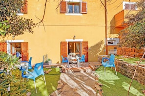 Un edificio amarillo con un patio que incluye una mesa, sillas, un muro de piedra y un pequeño jardín.