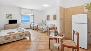 A bedroom with a bed, a desk, a chair, a refrigerator, and a window with a view. - Residence Argentiera Apartments (Sassari)
