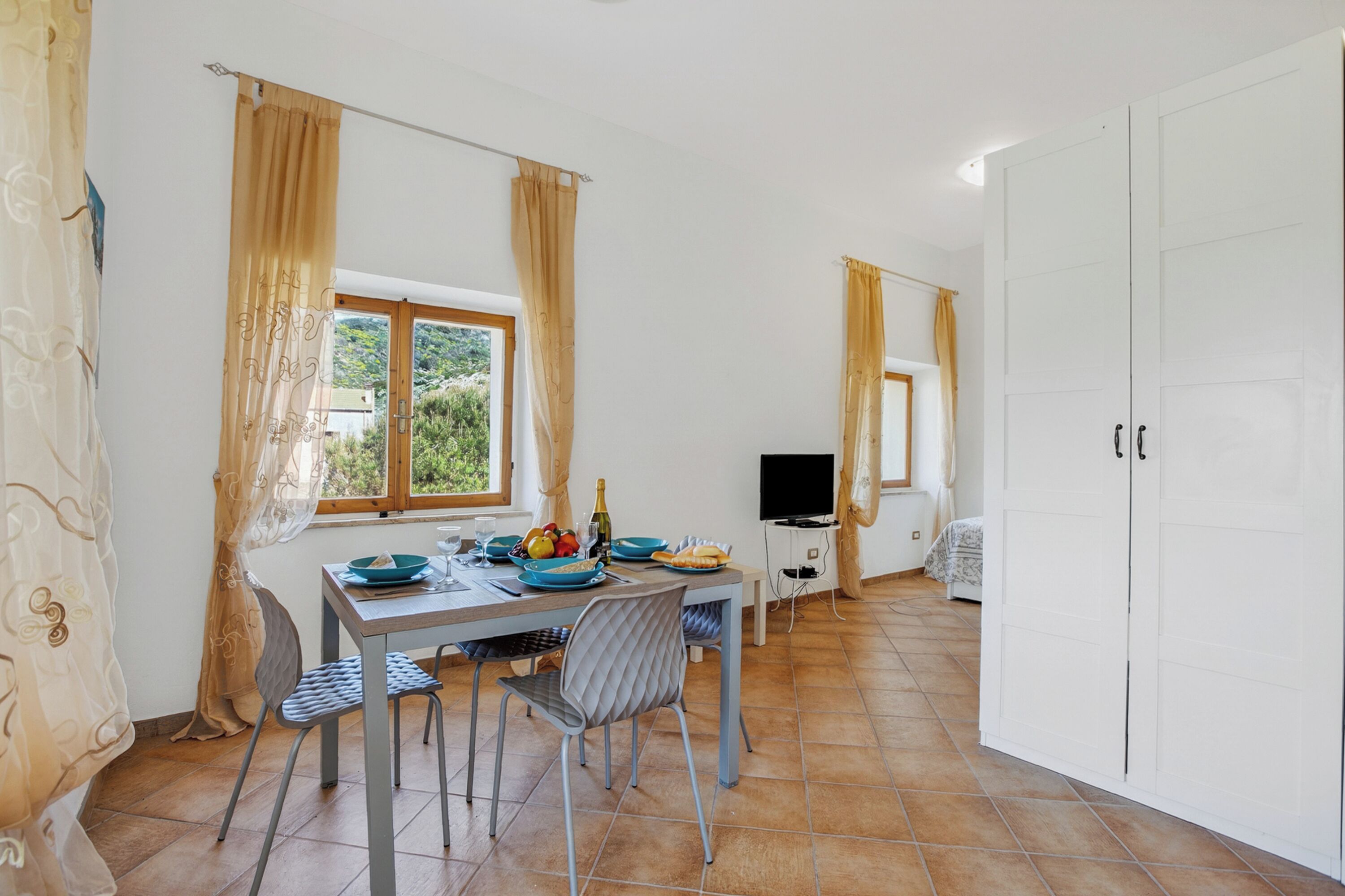 A dining area with a table set for two, a TV, and a wardrobe.