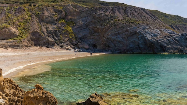 A coastal landscape with a beach, clear water, rocky cliffs, and a person walking on the shore. - Residence Argentiera Apartments (Sassari)