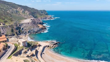 A coastal area with a beach, rocky cliffs, and a road leading to a building complex.