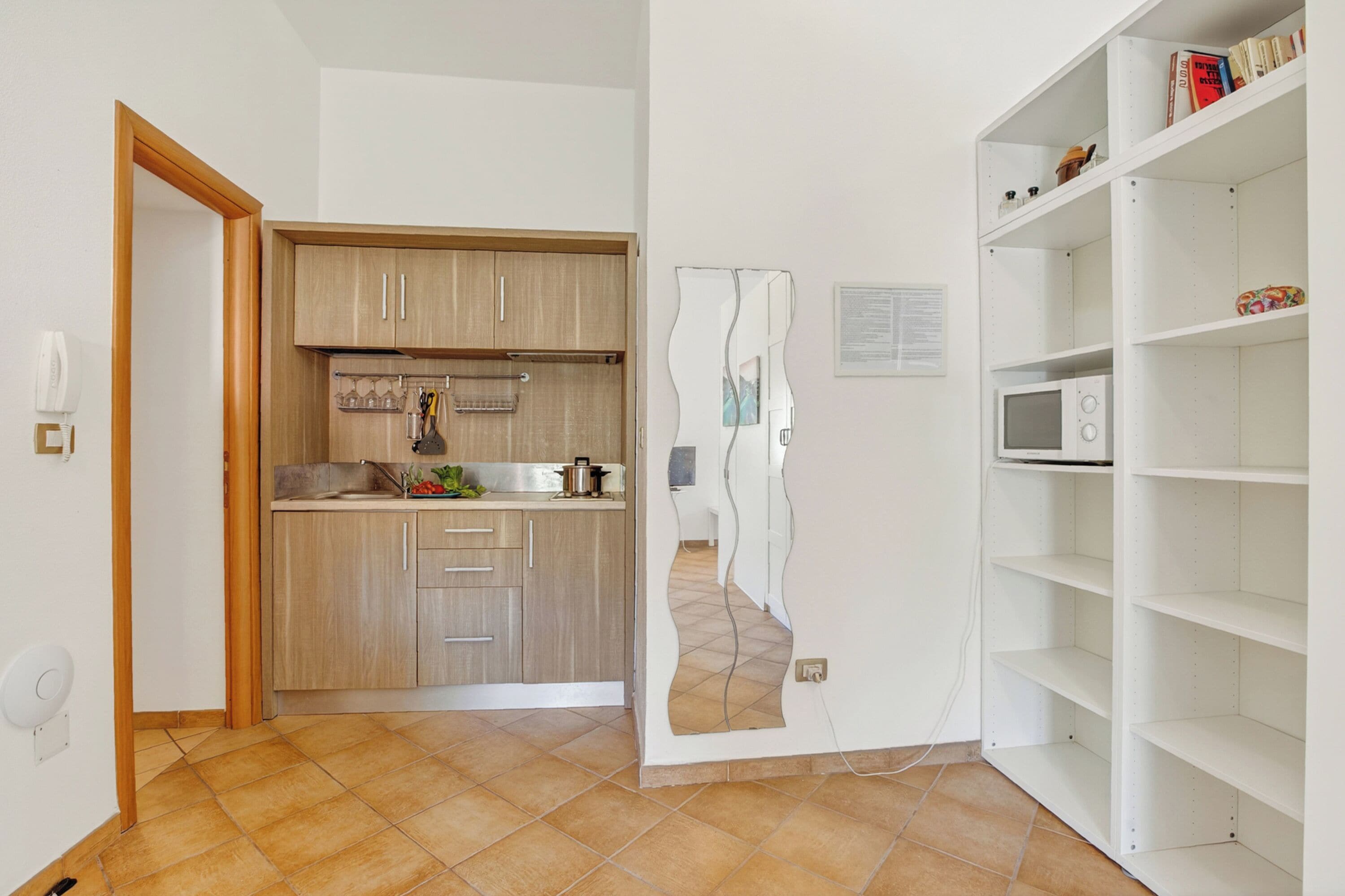 A kitchen with wooden cabinets, a microwave, and a white shelf unit.