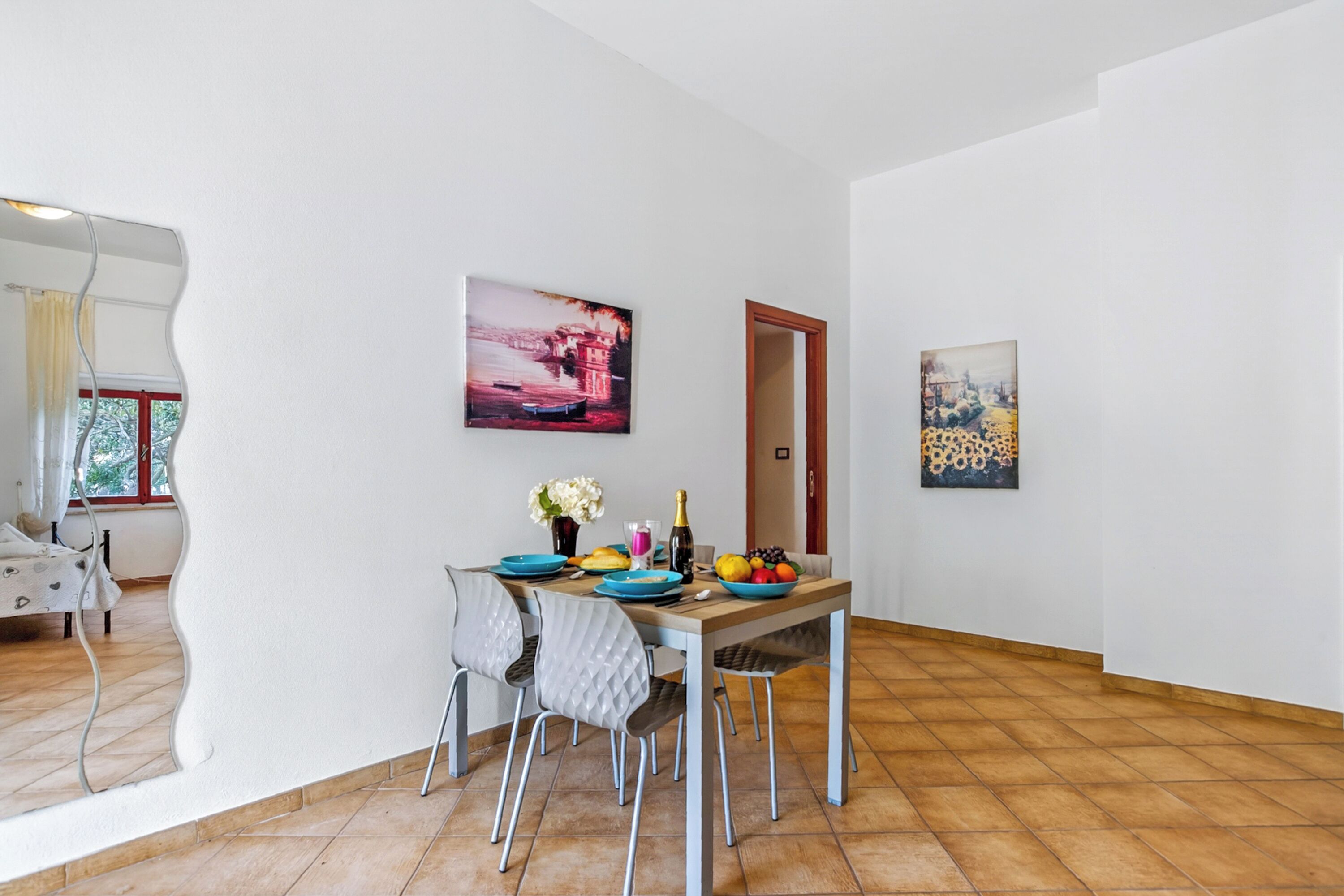 A dining area with a table set for two, chairs, a painting on the wall, and a door leading to another room.