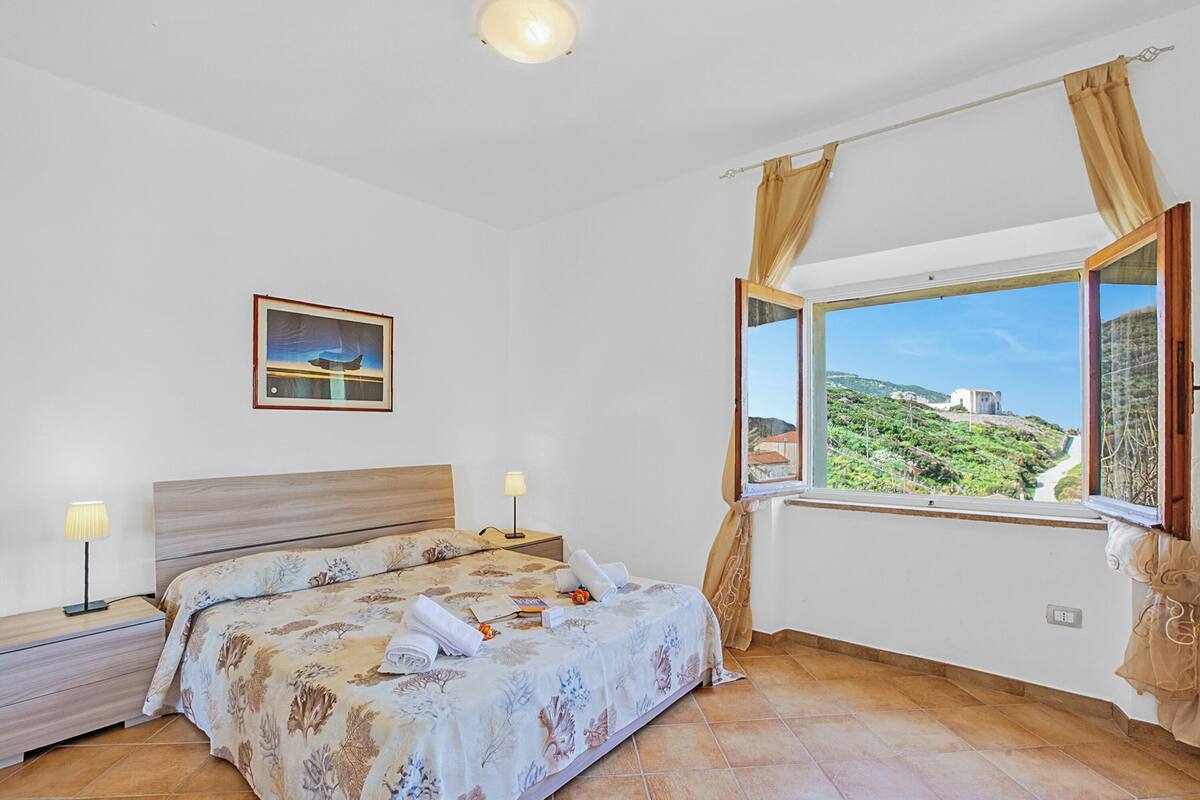 A bedroom with a bed, nightstands, a window with curtains, a painting on the wall, and a view of a landscape.