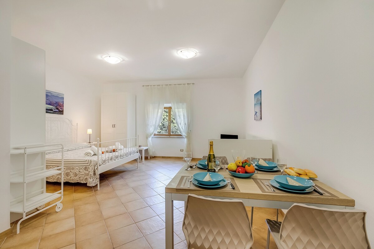 Una habitación con cama, una mesa de comedor con platos azules, una botella de champán y una ventana con cortinas.