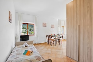 Una habitación con cama, una mesa de comedor con sillas, una ventana con cortinas y un armario de madera.