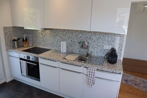 A modern kitchen with white cabinets, granite countertops, a built-in oven, a sink, and a coffee machine. - Apartment for vacation rental,1 BR, 1 BAR, kitchen, balcony Gaggenau/Baden-Baden (Gaggenau)
