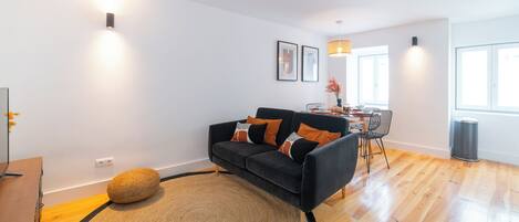A modern living room with a black sofa, a round rug, and a dining area with a table and chairs.