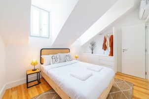 Un dormitorio moderno con techo inclinado, una cama de madera, una mesita de noche con lámpara y un armario con ropa colgada.